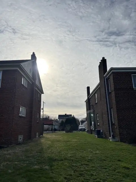 Sunlight pierces through the clouds, framed by suburban homes.
